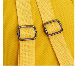 Detail of adjustable woven straps with gunmetal buckles on a yellow canvas backpack
