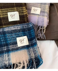Three different plaid tassel scarves with brand labels displayed on a flat surface