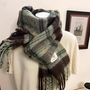 Detail of a thick plaid tassel scarf in green and brown with soft wool texture