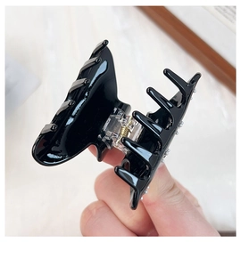 Detailed view of glossy black acrylic hair claw clip with rhinestone accents