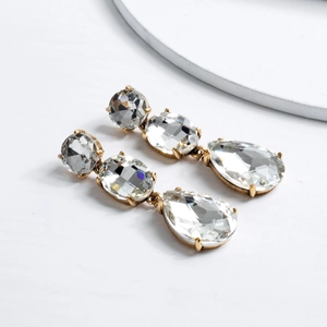 Close-up of golden tiered drop earrings with sparkling pear-shaped crystals and claw setting