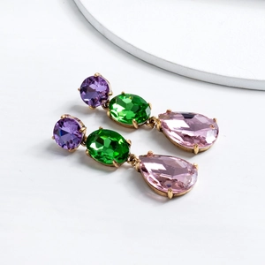 Macro detail of teardrop crystal earrings with purple, green, and pink stones in gold setting