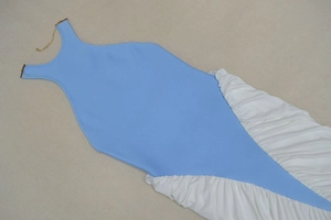 Detail of blue backless dress featuring a golden chain halter neck and white pleated hem