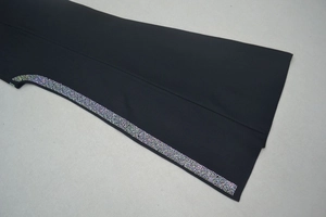 Détail d'une robe bandage noire avec bordure en strass multicolores sur le bord de la manche