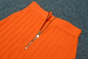 Detail aus hellorangem Rippstrick mit poliertem goldenem Metallreißverschluss am Bund