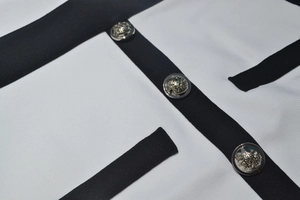 Détail macro du tissu texturé blanc avec bordure noire et boutons couronne argentés
