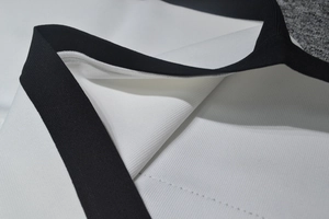 Détail de la robe en sergé blanc à col en V avec bordure côtelée noire et couture nette
