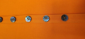 Detail view of orange knit dress with iridescent dark buttons on ribbed fabric