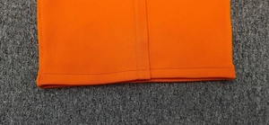 Detail shot of orange ribbed knit dress hem with high-quality stitching on grey background