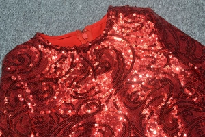 Détail d'une mini robe rouge à paillettes avec motifs tourbillons et fermeture éclair invisible