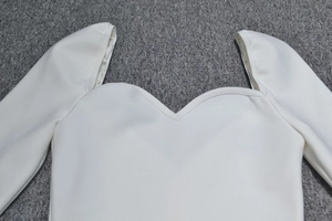 Détail d'une robe blanche à décolleté en cœur et manches longues sur un tapis gris foncé