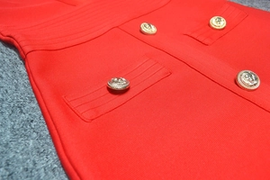 Detail eines roten Bandagekleids mit goldenen Löwenkopfknöpfen und Strukturstoff