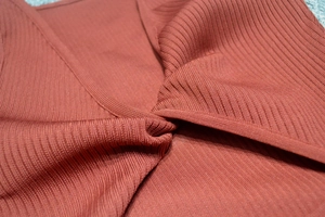 Detail of rust red ribbed knit fabric with twisted front design and elegant texture