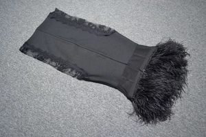 Detail of elegant black bandage dress featuring lace patchwork and lush feather trim