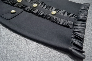 Detail of black knit dress with satin ruffles and elegant pearl gold-rimmed buttons