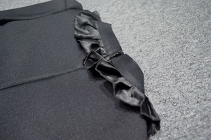 Detail of black ribbed knit dress featuring satin ruffle trim and invisible side zipper