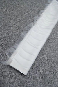 Detail of white pleated satin fabric and sheer mesh trim on off-shoulder bandage dress