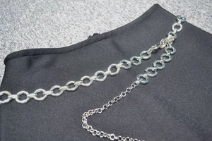 Détail d'une robe en maille noire avec des chaînes métalliques argentées à double couche