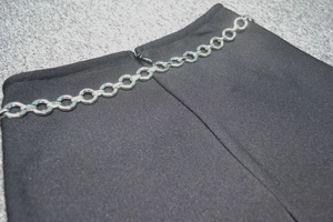Détail de la taille d'une jupe noire en maille avec chaîne en métal argenté et zip invisible