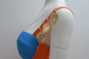 Close-up of vintage heart-shaped gold metal charms on orange shoulder straps of a dress