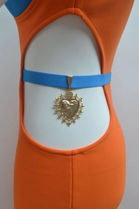 Detail of a golden heart pendant with vintage engraving on a blue strap over orange dress