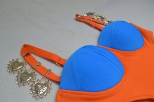 Detail of vibrant color-block top with golden heart-shaped hammered metal charms on straps