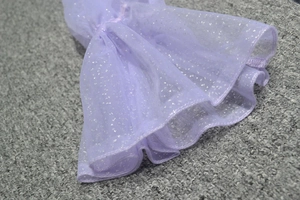 Détail du tissu en maille violette avec paillettes argentées et bord ondulé de la robe