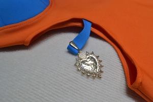 Detail of orange and blue swimwear featuring a gold heart pendant and textured fabric