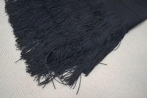 Detailansicht aus schwarzem Strickstoff mit eleganten, langen Fransenquasten
