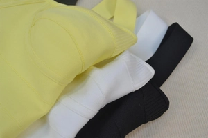Close-up of three layered bandage mini dresses in yellow, white, and black with fringe detail