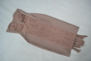 Detailed flat lay of a nude bandage dress featuring long tiered fringe and strapless cups