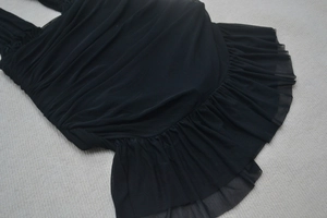 Detail of black halter dress showing intricate pleated mesh fabric and ruffled hemline