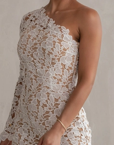 Detailed close-up of intricate white floral lace texture on a one-shoulder evening gown