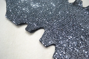 Detailed macro view of black sequin fabric with metallic shine and unique serrated edge design