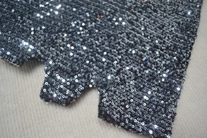Detailed view of black sequins fabric with metallic reflection and scalloped hem edge