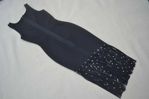 Détail d'une robe bandage noire sans manches montrant l'ourlet à franges et paillettes