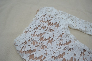 Detail of white floral lace fabric with nude lining on elegant one-shoulder dress