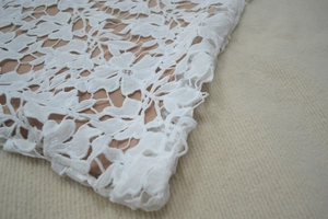 Detailed close-up of premium white floral lace fabric with a soft beige inner lining layer