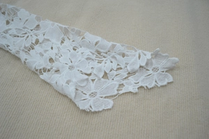 Close-up of white floral lace trim with hollowed-out petal details on dress fabric