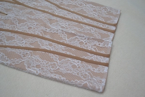 Détail de dentelle florale blanche sur tissu rose avec ruban marron et fermeture éclair en métal