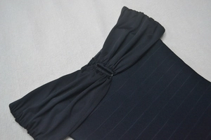 Gros plan sur l'encolure froncée et le tissu côtelé noir de la robe bandage chic
