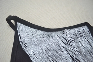 Détail des franges argentées sur l'encolure d'une robe bandage noire sans manches