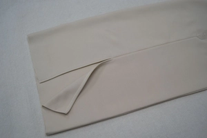 Détail de la fente de l'ourlet sur une robe de soirée bandage beige sans manches