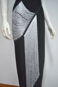 Détail d'une robe bandage noire avec de longues franges et pompons argentés métalliques