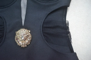 Detail of V-neck mesh paneling dress featuring a golden lion head metallic emblem