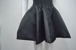 Détail de la robe satinée noire à ourlet bouffant avec plis structurés et empiècements