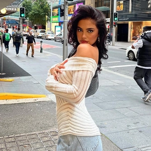 Detailed texture of white off-the-shoulder long sleeve knit top in urban street setting