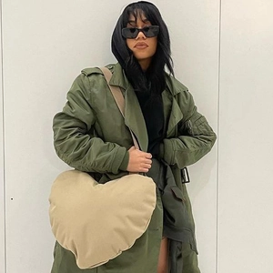 Grand sac bandoulière en peluche kaki en forme de cœur porté par un mannequin en manteau