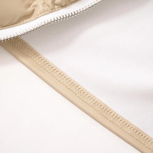 Détail macro du gilet matelassé beige avec fermeture éclair blanche et couture renforcée