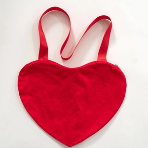 Vue détaillée d'un sac à bandoulière rouge en forme de cœur avec sangle large et zip
